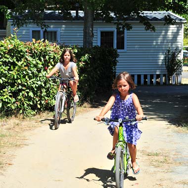 Enfants à vélo devant un mobile en location au camping dans les Landes à Messanges