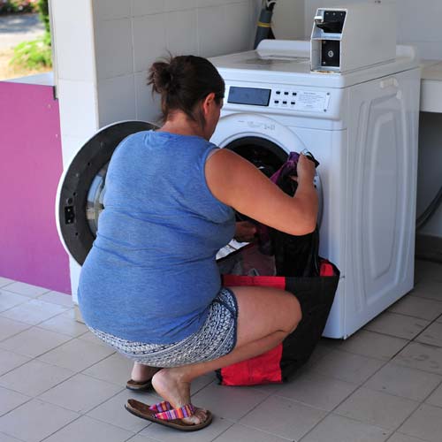Campeuse mettant son linge dans la machine à laver du camping dans les Landes
